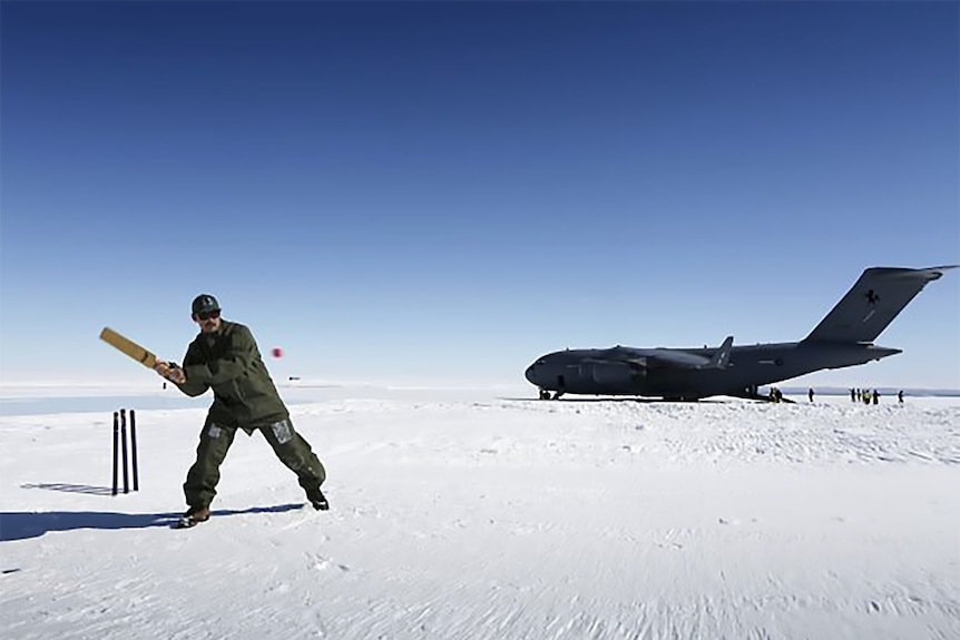 A man plays cricket on the ice in Antarctica in front of a military plane