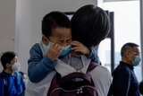 A child being held by a woman cries as he waits in line to board a plane.
