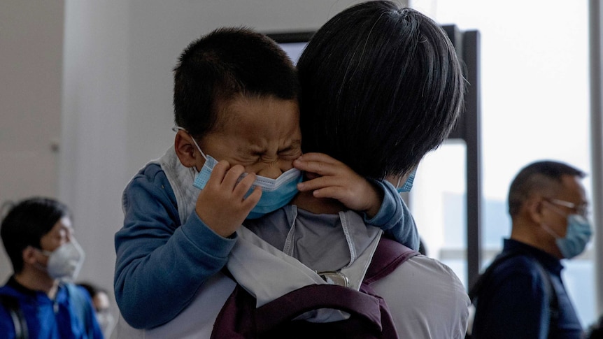 A child being held by a woman cries as he waits in line to board a plane.