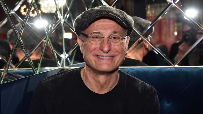 Swedish Actor Michael Nyqvist sitting in front of a mirrored wall.