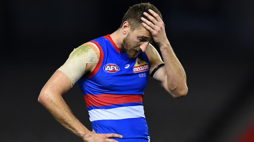 A Western Bulldogs AFL player holds his left hand to his forehead after a loss to Port Adelaide.