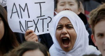 A girl holds a sign reading "am I next" as she yells from the crowd.