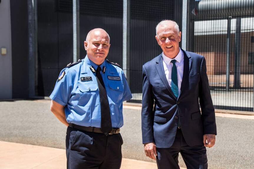 Two men in high-ranking roles standing outside prison walls.