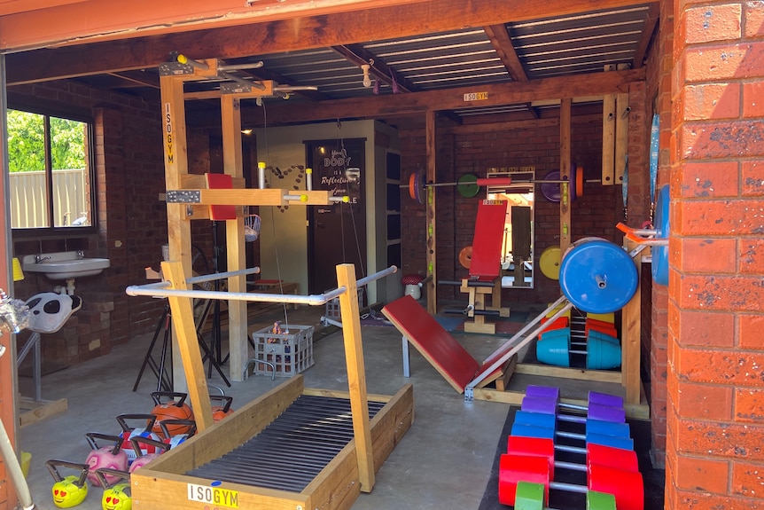 A garage full of colourful gym equipment, including a timber treadmill and timber pull up bar.