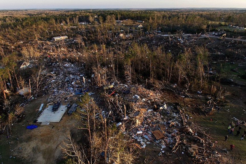 Debris from flattened homes is scattered throughout several clearings among trees.