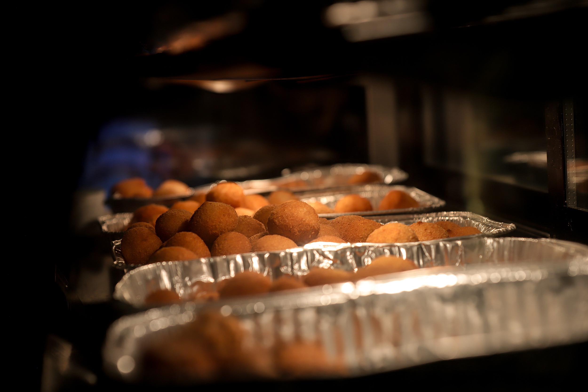 Trays of fried cheese balls in a bain mairie under a warming light