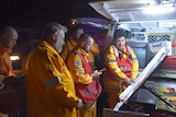 Queensland Rural Fire Brigade volunteers stand behind a vehicle at night assessing bushfire conditions.