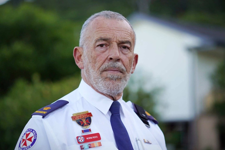 A man wearing a New South Wales ambulance uniform stands and stares into the camera.