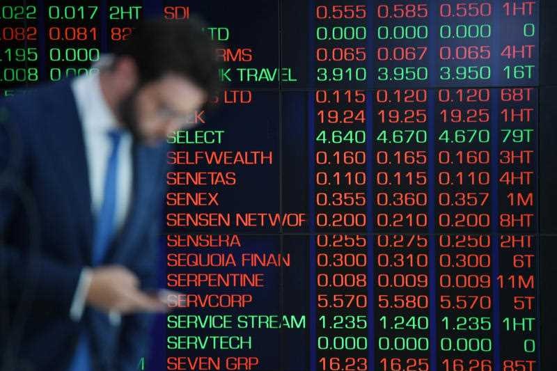 A man checks his phone in front of market trading boards on show at the Australian Securities Exchange