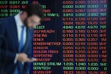 A man checks his phone in front of market trading boards on show at the Australian Securities Exchange