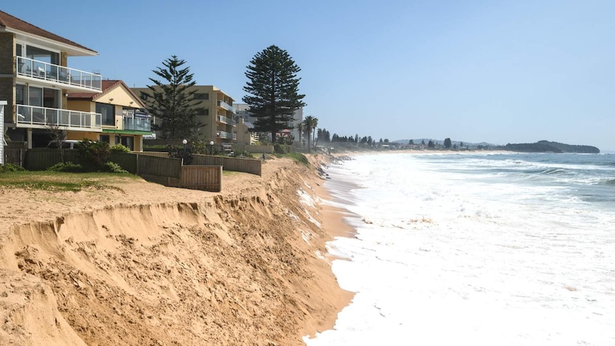 a home at the edge of a sand cliff with white foamy waves below