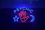 A blue and red neon sign spells 'psychic' above a lit up star, moon and hand