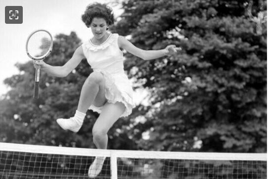 black and white photo of woman jumping over tennis net