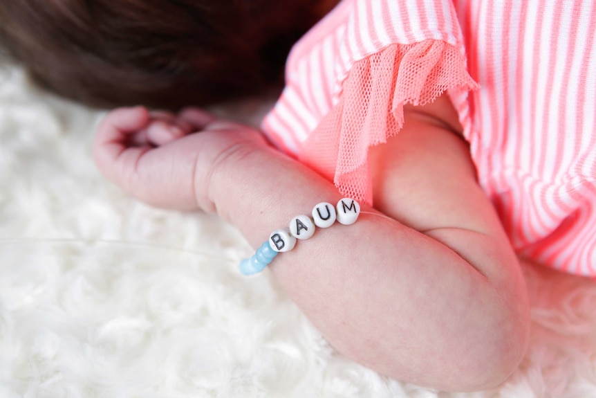 A baby wearing a bracelet with her surname Baum on it.