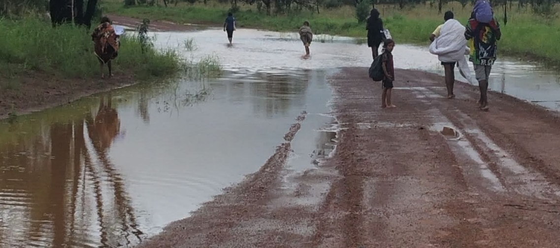 Un grupo de personas caminando por charcos mojados en una carretera roja