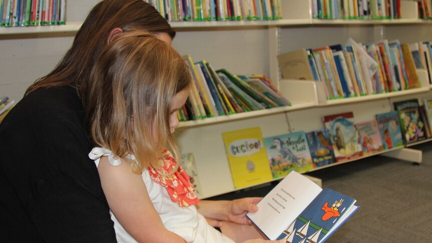 A mother reads to her daughter at the library