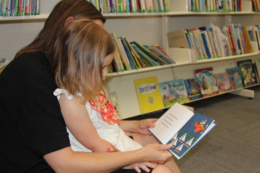 A mother reads to her daughter at the library