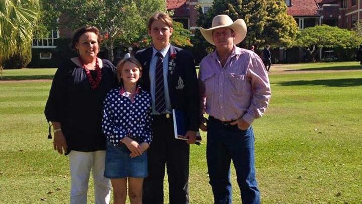 a family standing on grass with a school building behind.