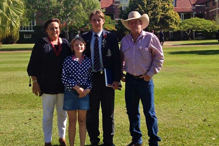 a family standing on grass with a school building behind.