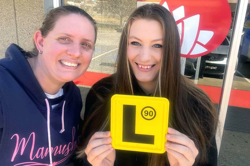 A mother and daughter smiling with a L plate.