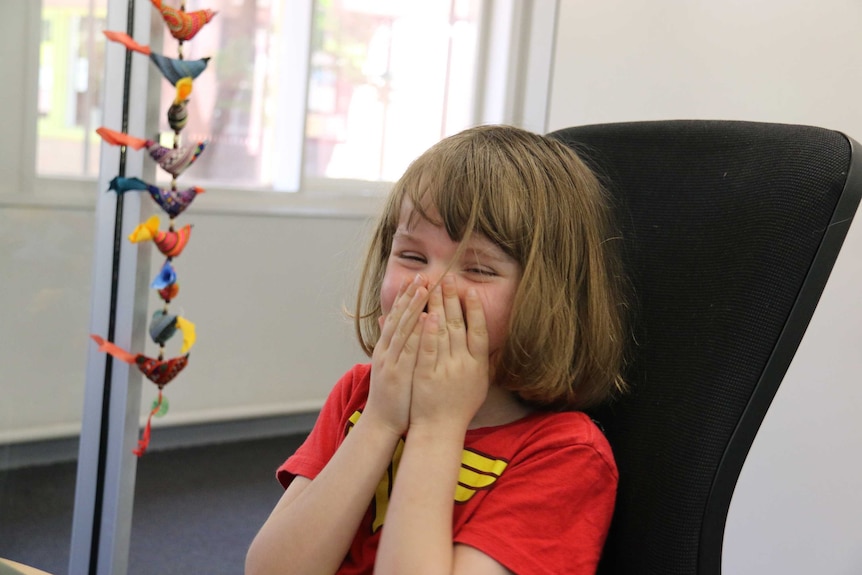 A laughing girl puts her hands to her mouth.