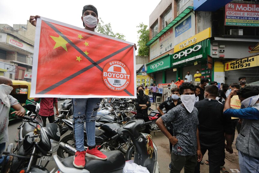 A man wearing a mask and standing on a car holds a sign with the Chinese flag crossed out