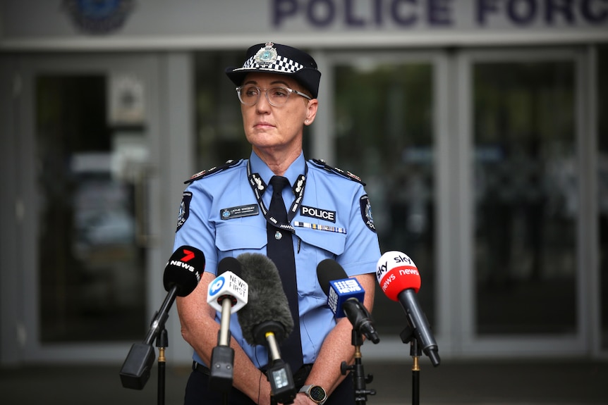 A woman police officer stands in front of microphones.