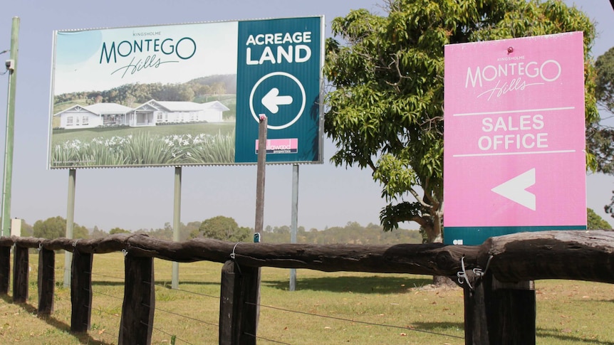 Two signs advertising Montego Hills 'acreage land' and 'sales office' stand on grass behind a timber fence.