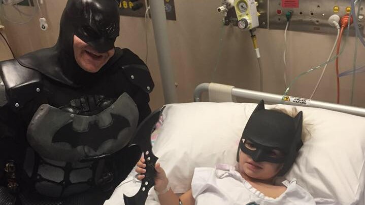 Eamon Obst in a hospital bed getting a visit from Batman.