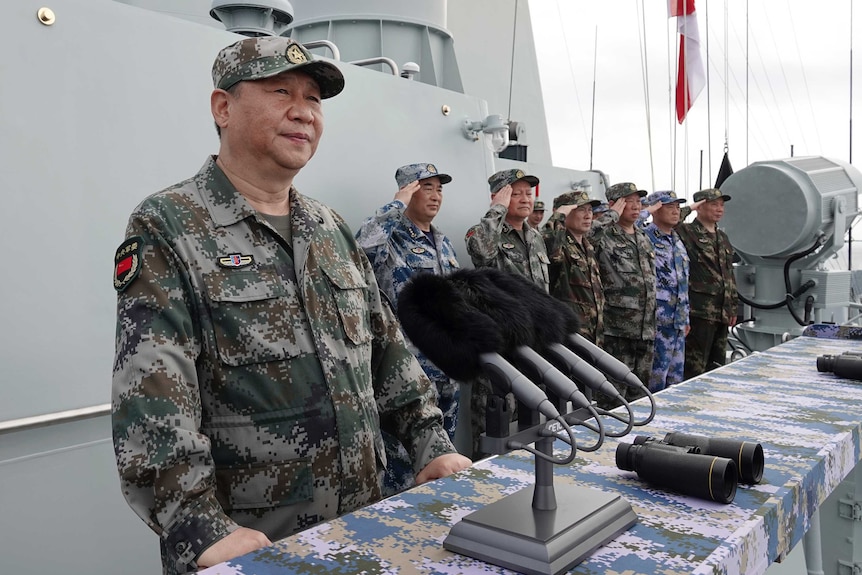 Xi Jinping, îmbrăcat într-o uniformă a armatei petroliere, maro și verde, vorbește pe o navă după ce a analizat marina.