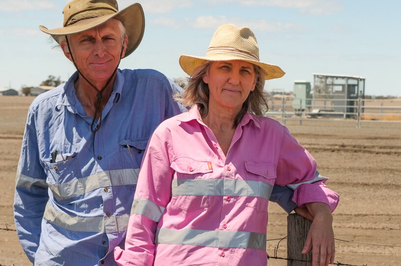 Zena and Gary Ronnfeldt stand along a fence on the property boundary with a gas well in the background, Dalby, Queensland 2020.