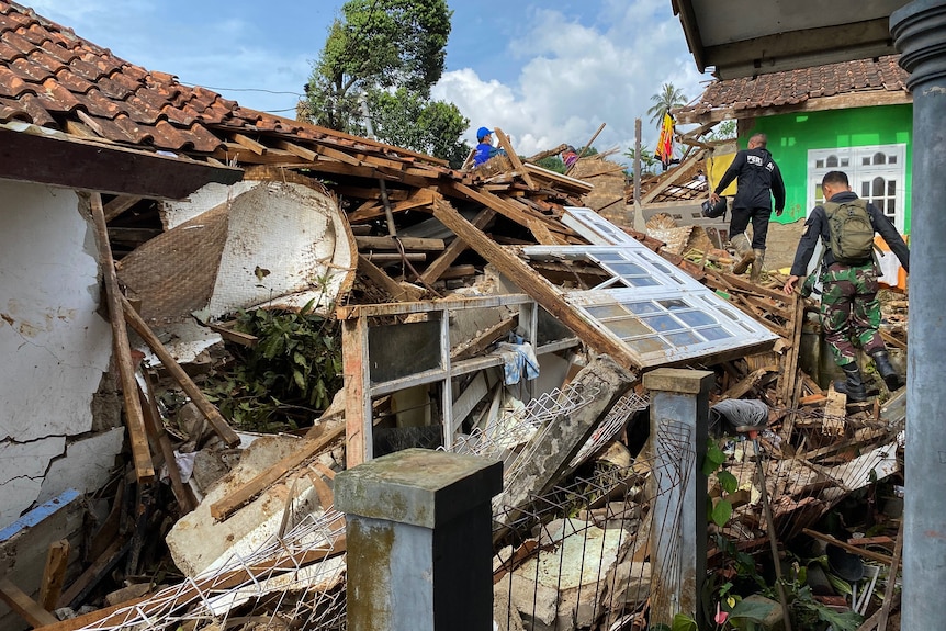 Volunteers walk over piles of rubble out the front of a destroyed house