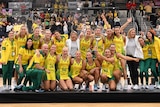 Aussie Diamonds players stand on stage with the trophy and arms around each other as fireworks go off behind them