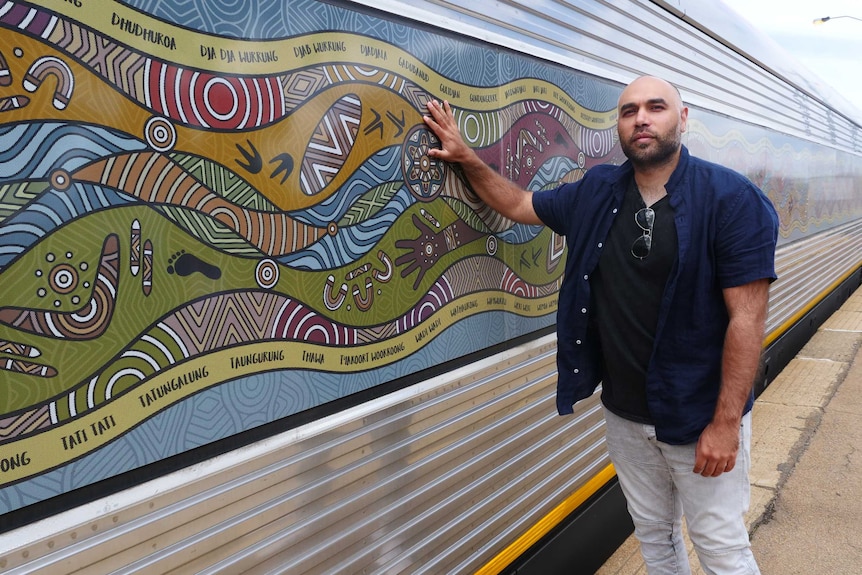 A man stands in front of train with an Indigenous design on the windows.