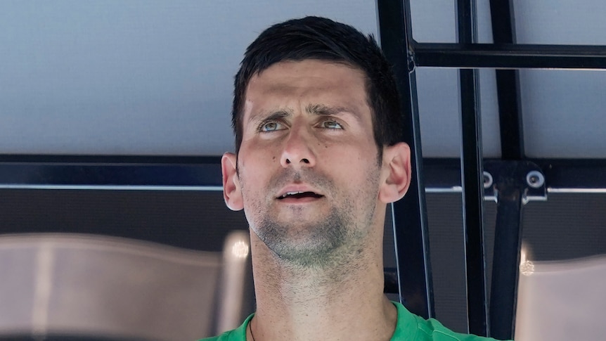 Novak Djokovic looks on while seated on a practice court