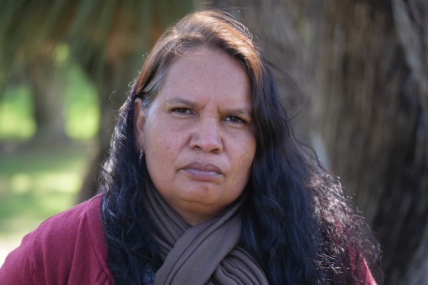 MCU of Megan Krakouer wearing pink cardigan and brown scarf, looking straight at the camera.