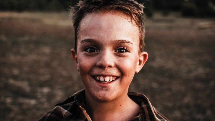 A young boy with dirt on his face smiles at the camera