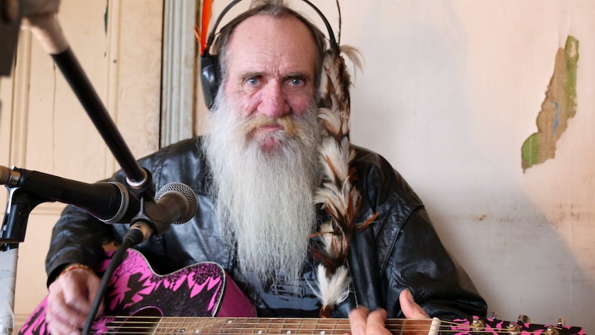 Leon Bozanich looking at the camera while playing the guitar and singing into a microphone.