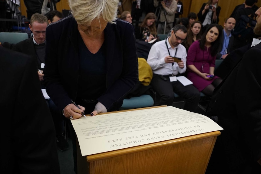 A woman signs a large document detailing a nine-country memorandum on disinformation on Facebook.