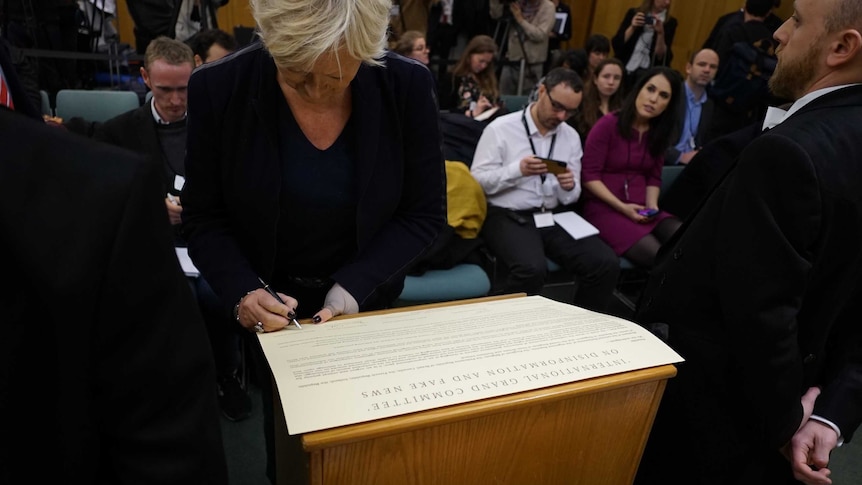 A woman signs a large document detailing a nine-country memorandum on disinformation on Facebook.