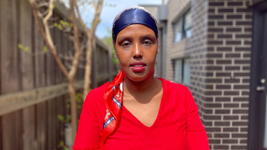 A woman wearing a headscarf standing behind a house. 