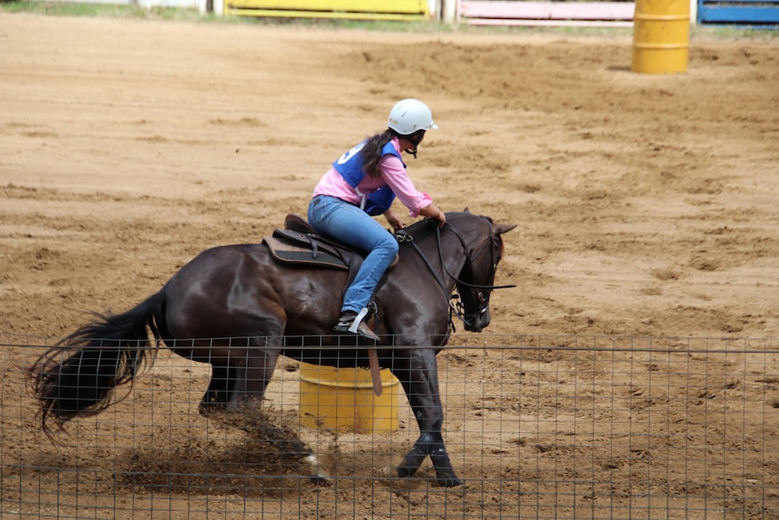 A young woman on a black horse ducks low as they weave around a barrel