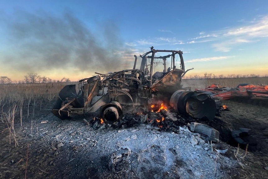 A burnt tractor, still smoking after being hit by a bomb. 