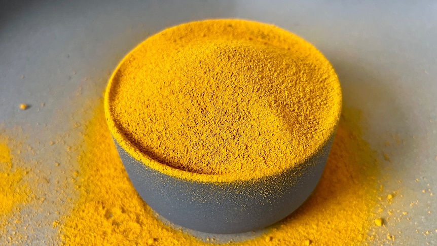 yellow turmeric powder overflowing in a round grey bowl with powder on the table around the bowl