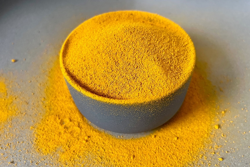 yellow turmeric powder overflowing in a round grey bowl with powder on the table around the bowl