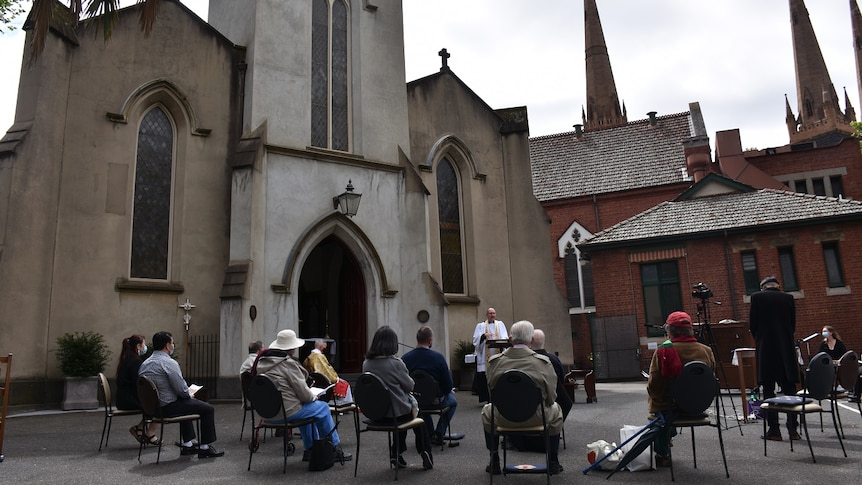 Twenty parishoners gather outside a church on distanced seats for an outdoor mass service.
