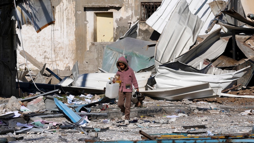 A young child walks among rubble from buildings that have been destoryed.