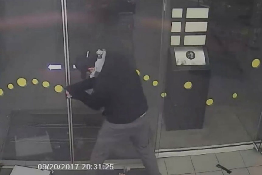 A thief tries to force his way out of the petrol station he robbed.