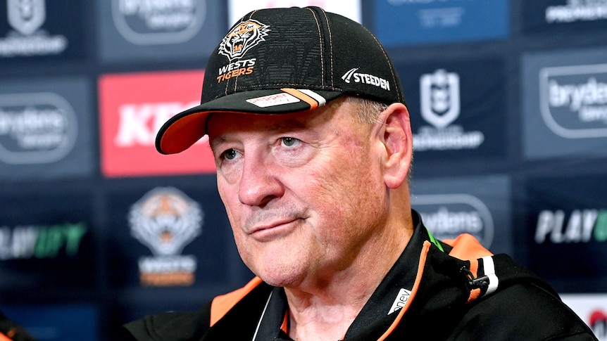 A man in a baseball cap fronts the media at a press conference.