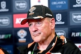 A man in a baseball cap fronts the media at a press conference.
